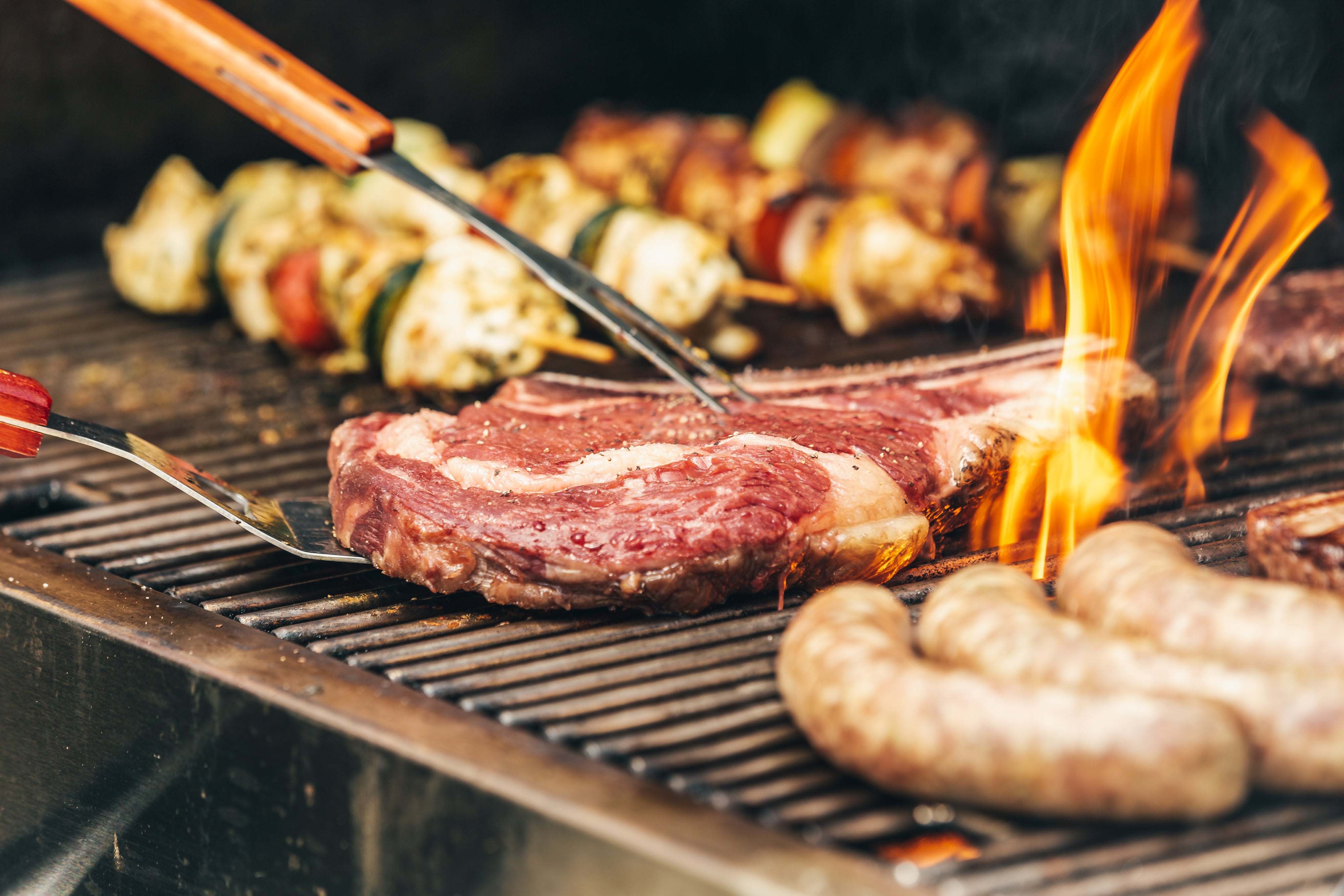 Sicht auf einen Grill mit Würsteln, Steak und Spießen
